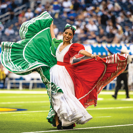Female dancer twirling the skirt of a red, white and green dress.